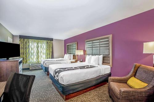 科尔尼La Quinta by Wyndham Kearney的酒店客房设有两张床和紫色墙壁。