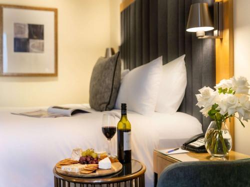 悉尼索菲特悉尼温特沃什酒店的酒店客房,配有一张床和一盘食品及葡萄酒