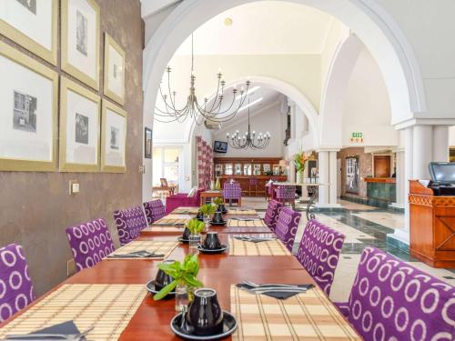 约翰内斯堡约翰内斯堡兰德堡美居酒店的一间长餐厅,配有紫色的椅子和桌子