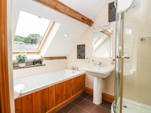 Acton ScottThe Olde Cowshed的一间带水槽和浴缸的浴室以及窗户。