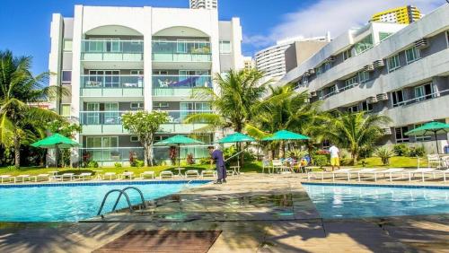 纳塔尔Apart Ponta Negra Beach Natal -Lovely Flat的大楼前带桌子和遮阳伞的度假游泳池