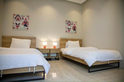 吉达شاليهات المرفأ Almarfa Resort的一间卧室配有两张床和一张桌子上的两盏灯。