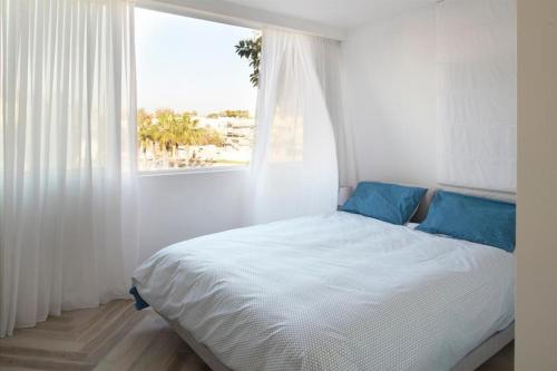 荷兹利亚Luxury SeaSide DeShalit Square的白色客房的一张带蓝色枕头的床,配有窗户