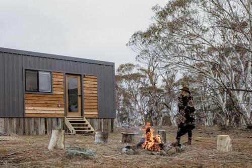 金德拜恩Big Yard Escapes - Two Off-Grid Tiny Houses on the Mowamba River的站在小屋前的火旁的人