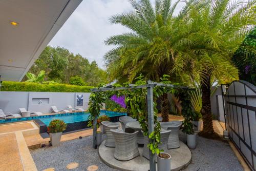 Ban Khlong Haeng3 Bedroom Platinum Pool Villa Smooth as Silk的一个带椅子、棕榈树和游泳池的庭院