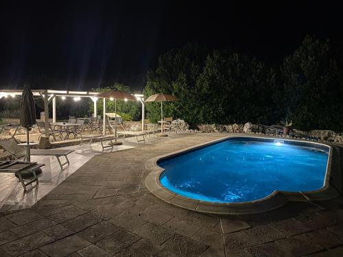 卡尔皮尼亚诺萨伦蒂诺Agriturismo Masseria Saittole的夜间游泳池,配有桌子和遮阳伞
