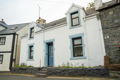 波特帕特里克The Portpatrick Pad - A cosy 3 bed cottage, w. sea views & garden office的白色的房屋,设有蓝色的窗户