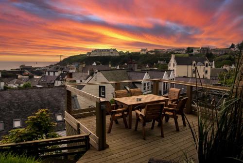 波特帕特里克The Portpatrick Pad - A cosy 3 bed cottage, w. sea views & garden office的日落时分带木桌和椅子的甲板