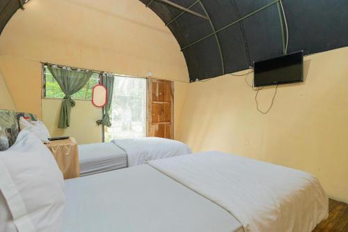 JunggoChikar Glamping At Wisata Coban Talun Mitra RedDoorz的一间卧室设有两张床、一台电视和一扇窗户。
