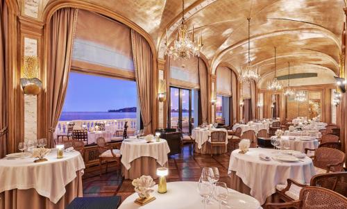 滨海博利厄La Réserve de Beaulieu的餐厅设有白色的桌椅和大窗户