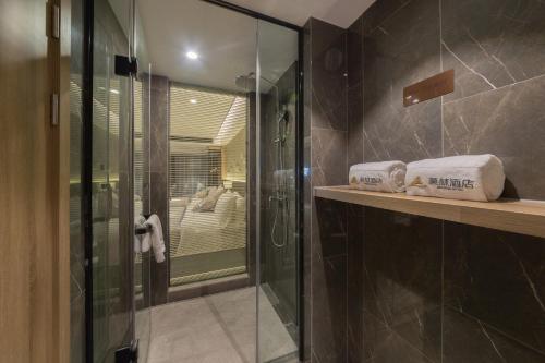 无锡莫林酒店无锡江南大学融创文旅城店的浴室设有玻璃淋浴间,并在柜台上备有毛巾