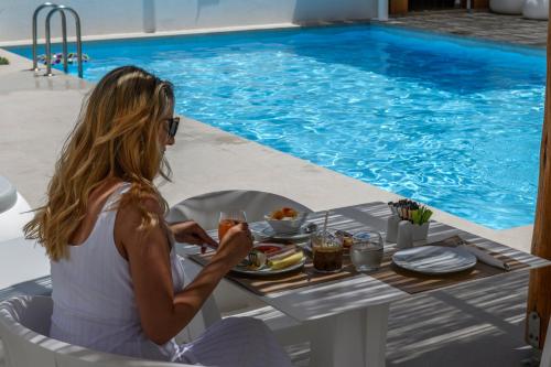 阿诺梅拉Mykonaki Hotel的坐在桌边的女人,在泳池边用餐