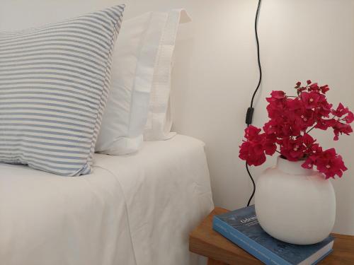 米尔芳提斯城Estúdio Lagoa Azul的一张桌子上摆放着红色花卉的花瓶,床边摆放着