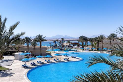 赫尔格达The V Luxury Resort Sahl Hasheesh的一个带蓝色遮阳伞和椅子的游泳池以及大海