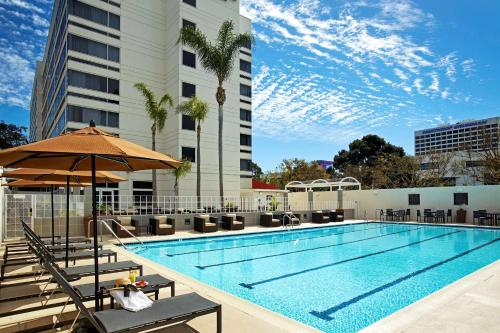 埃尔塞贡多LAX希尔顿逸林酒店-埃尔塞贡多的一座带椅子和遮阳伞的游泳池位于大楼旁