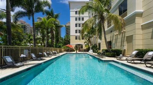 棕榈滩花园棕榈滩花园希尔顿花园酒店的一座带椅子和棕榈树的游泳池以及一座建筑