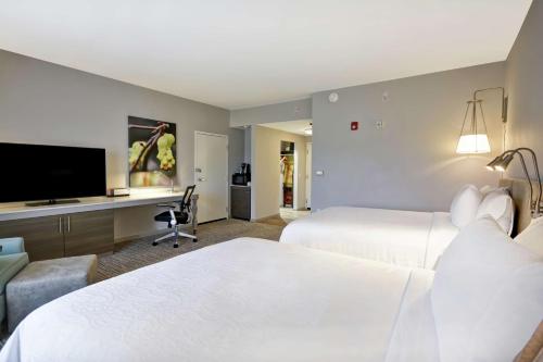加斯托尼亚Hilton Garden Inn Gastonia的酒店客房设有两张床、一张书桌和电视