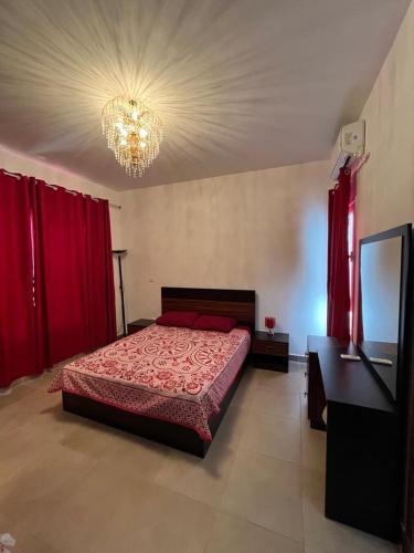 Dawwār Ruḩayyimamwaj的一间卧室配有一张带红色窗帘和吊灯的床。
