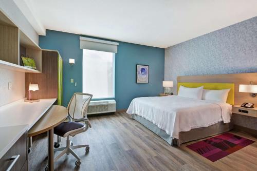 西棕榈滩Home2 Suites By Hilton West Palm Beach Airport的酒店客房,配有一张床、一张桌子和椅子