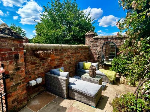 约克Tanyard Cottage - Whixley, York, North Yorkshire的砖墙,带两把藤椅和沙发