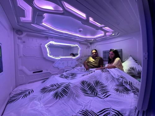 马拉加GOOD VIBES ONLY Capsule Hostel Malaga的坐在紫色房间床上的男人和女人