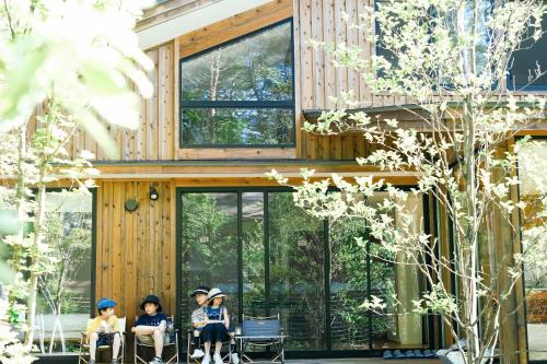 轻井泽Karuizawa Forest Seasons Villa的一群人坐在房子前面的椅子上