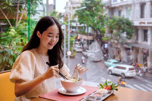 胡志明市Sheraton Saigon Grand Opera Hotel的坐在桌子上吃一碗食物的女人