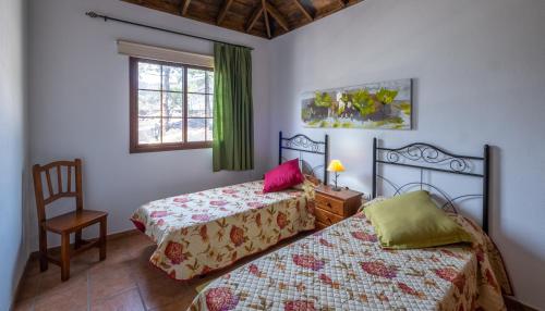 埃尔帕索Casa piscina y naturaleza en La Palma的一间卧室设有两张床、一把椅子和一个窗户。