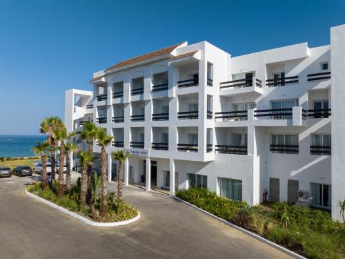 玛丽娜斯米尔PLAYA DEL PACHA Suites Hotel的一座白色的建筑,在海洋前方种有棕榈树