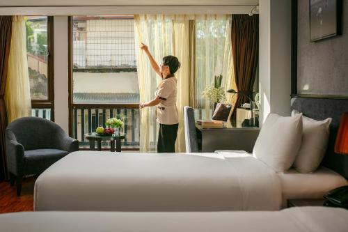 河内Hanoi La Palm Premier Hotel & Spa的女人在向酒店房间的窗户看