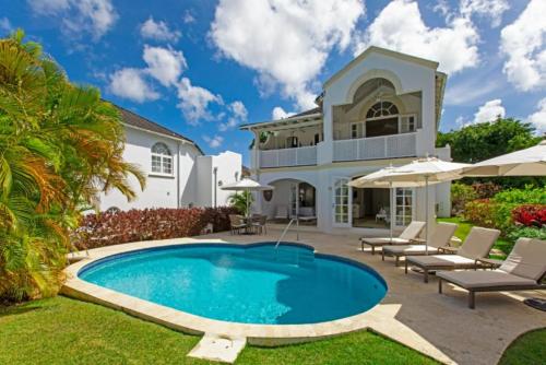 圣詹姆斯Royal Westmoreland, Royal Villa 1 by Barbados Sothebys International Realty的游泳池位于带椅子和遮阳伞的房子前