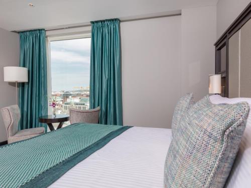 贝尔法斯特Grand Central Hotel Belfast的一间卧室设有床铺和一个带绿色窗帘的窗户。