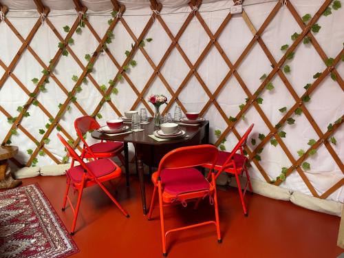新港The Yurts at Burnt House Farm的蒙古包内带红色椅子和桌子的用餐室