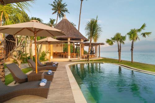 珀尼达岛The Sankara Beach Resort - Nusa Penida的一个带椅子和遮阳伞的游泳池的度假酒店