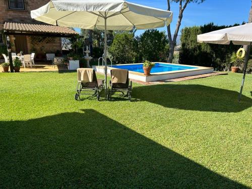 马拉加Casa Rural Cupiana Piscina privada Malaga的庭院里设有两把椅子和一把遮阳伞,庭院里设有游泳池