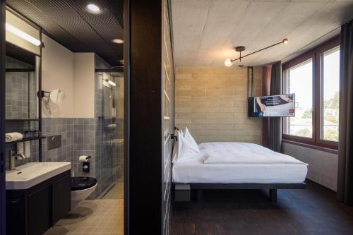 圣加仑Tailormade Hotel LEO St Gallen的一间卧室配有一张床,浴室配有电视。