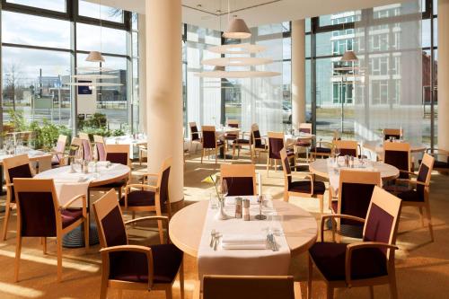 柏林Essential by Dorint Berlin-Adlershof的餐厅设有桌椅和大窗户。