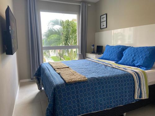 瓜拉久巴Flat Guarajuba, Charmoso Porto Smeralda的一间卧室配有一张带蓝色棉被的床和窗户。