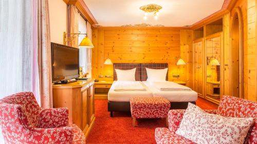 奥伯斯特多夫Alpenhotel Oberstdorf - ein Rovell Hotel的一间卧室配有一张床、两把椅子和电视