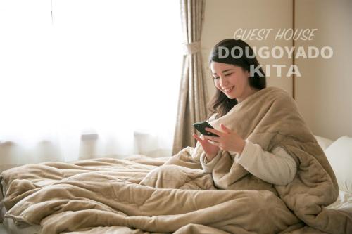松山GUEST HOUSE DOUGOYADO KITA - Vacation STAY 14923的躺在床上看手机的女人