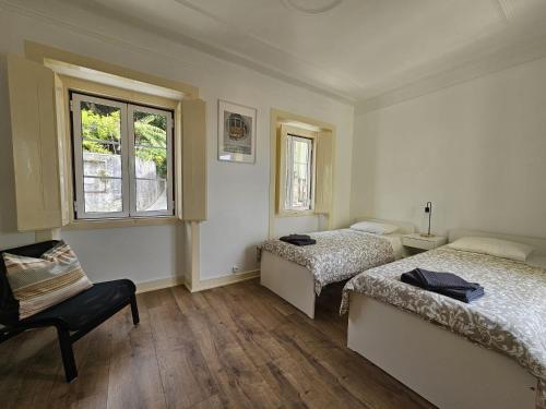辛特拉Maria Saudade Apartamento的一间卧室设有两张床、一把椅子和一个窗户。