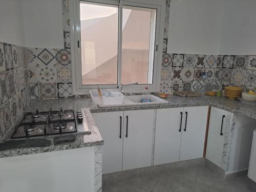 KerkoueneDar El Yasmine 2的厨房配有白色橱柜、水槽和窗户。