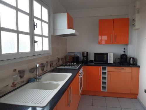 巴斯特尔Les ptits flamboyants的厨房配有橙色橱柜、水槽和窗户。