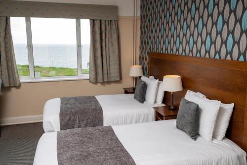伯恩茅斯Commodore Hotel by Greene King Inns的酒店客房设有两张床和窗户。