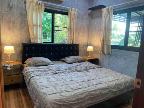 Ban Si WichaBan Aob Maiy(บ้านโอบไม้)的一间卧室配有一张带两盏灯的床和两扇窗户。