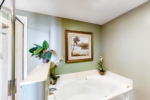 沃尔顿堡滩Waters Edge 310的浴室设有白色浴缸和墙上的绘画作品