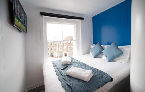 卢顿CiTi Hotel London Luton的蓝色的客房配有带枕头的床和窗户。
