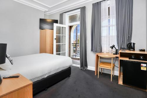 悉尼Penshurst Hotel的配有一张床、一张书桌和一扇窗户的酒店客房
