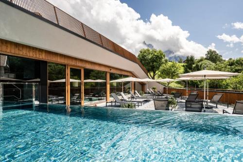 卡斯特尔罗托阿尔彭皇家酒店的一座带椅子和遮阳伞的游泳池位于一座建筑旁边