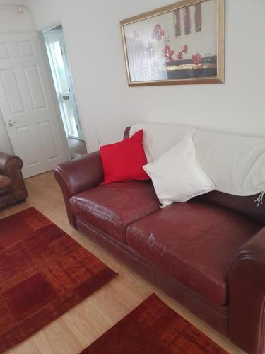 马斯顿格林Quiet house 8 mins from NEC/AIRPORT的客厅配有棕色皮沙发,提供红色和白色枕头